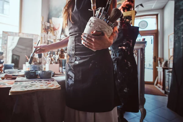 Talentovaný umělec v dílně míchá vybarvení pro její nový projekt, zatímco drží sklenici s kartáči — Stock fotografie