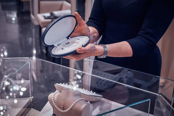 Zarif kuyumcu lar yardımcısı müşteri için durumda güzel inci kolye gösteriyor