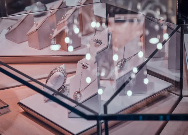 Variety of beautiful gold ornamentations on the white display under the glass in jewellery shop — Stock Photo, Image