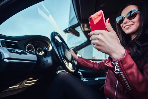 Genç ve güzel bir kadın arabasında oturmuş cep telefonuyla sohbet ediyor.