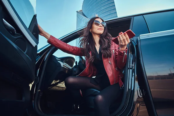 아름다운 똑똑한 여자는 휴대 전화에 채팅하는 동안 그녀의 새로운 차에 포즈를 취하고있다 — 스톡 사진