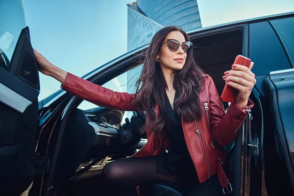 Hermosas mujeres inteligentes está posando en su nuevo coche mientras chatea en el teléfono móvil — Foto de Stock