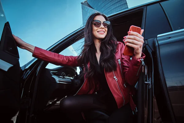 Hermosas mujeres sonrientes está posando en su nuevo coche mientras chatea en el teléfono móvil — Foto de Stock