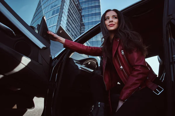Donne attraenti è in posa nella sua nuova auto. Indossa una giacca di pelle rossa. . — Foto Stock