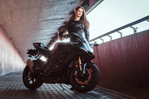 Giovane donna attraente è in piedi in galleria con la sua moto e casco — Foto Stock