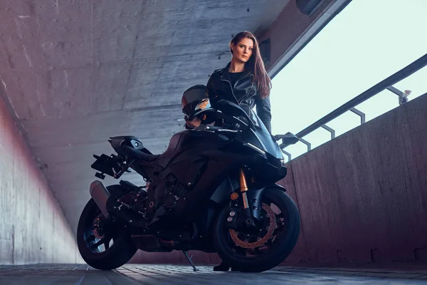 Giovane donna attraente è in piedi in galleria con la sua moto e casco — Foto Stock