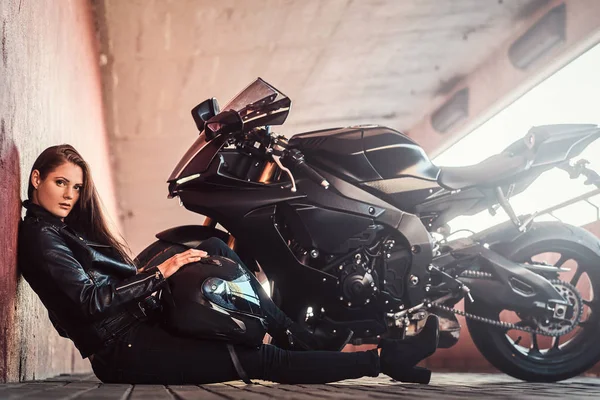 Beautiful serious woman is sitting near her bike in tunnel and leaning on wall — Stock Photo, Image