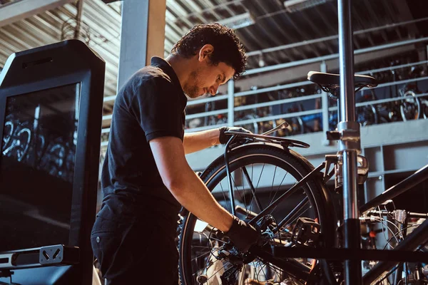 Attractive mechanic is fixing customers bicycle at his own workshop.