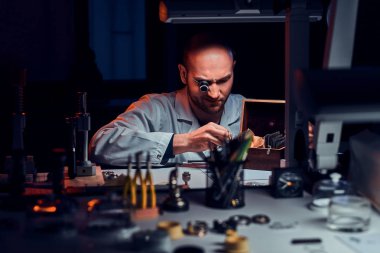 Odaklanmış adam monocle ve diğer araçları eski saatler tamir ile atölyesinde çalışıyor