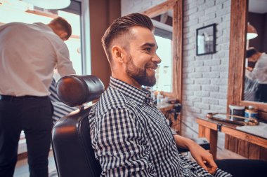 Meşgul berber dükkanında bir berber beklerken çekici bakımlı adam oturuyor