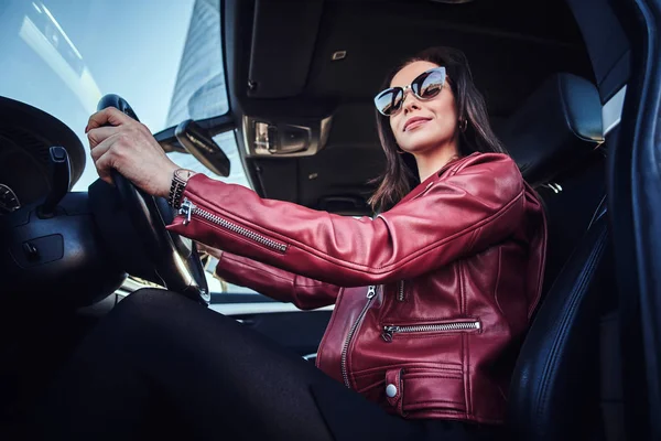 Atractiva joven en chaqueta roja y gafas de sol en la conducción de su coche — Foto de Stock
