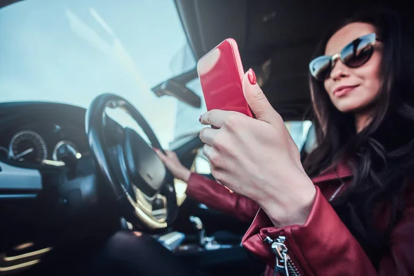 Giovane bella donna si trova nella sua auto mentre chatta sul telefono cellulare — Foto Stock