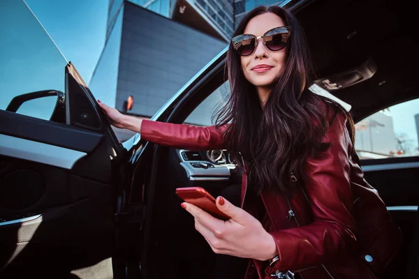 Hermosas mujeres sonrientes está posando en su nuevo coche mientras chatea en el teléfono móvil —  Fotos de Stock
