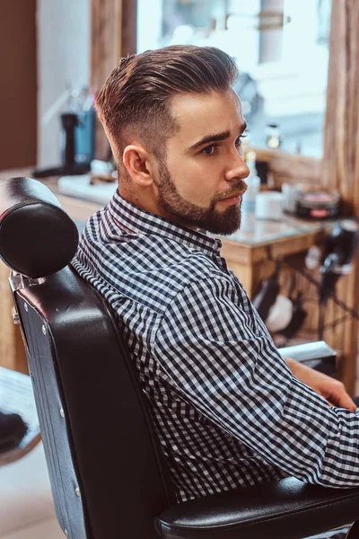 Aantrekkelijke peinzende man wacht op zijn beurt om een kapsel te krijgen bij drukke Barbershop — Stockfoto