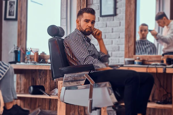 Atraente homem pensativo está esperando por sua vez para cortar o cabelo na barbearia ocupada — Fotografia de Stock