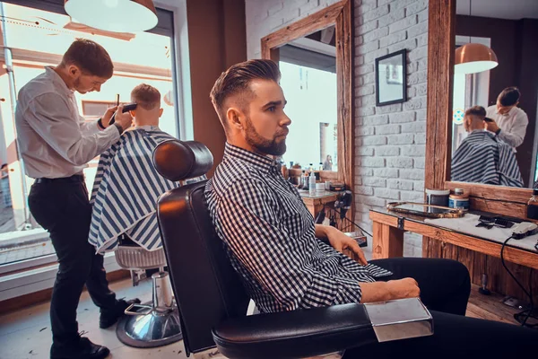 Atraente homem pensativo está esperando por sua vez para cortar o cabelo na barbearia ocupada — Fotografia de Stock