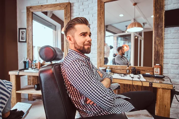 Homem bonito preparado está esperando por sua vez para cortar o cabelo na barbearia ocupada — Fotografia de Stock