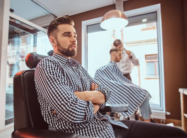 Homem bonito preparado está esperando por sua vez para cortar o cabelo na barbearia ocupada — Fotografia de Stock