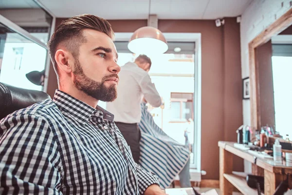 Groomed handsome man is waiting for his turn to get a haircut at busy barbershop — Stock Photo, Image