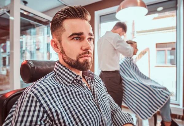 Hombre guapo arreglado está esperando su turno para cortarse el pelo en la peluquería ocupada — Foto de Stock