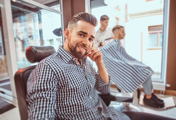 Atrakcyjny zadbany człowiek siedzi podczas oczekiwania na fryzjera w zajęty Barbershop — Zdjęcie stockowe