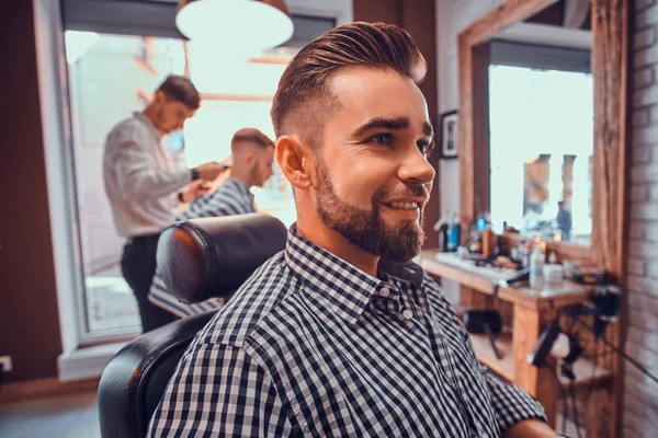 Aantrekkelijke geprepareerde man zit tijdens het wachten voor een kapper bij drukke Barbershop — Stockfoto