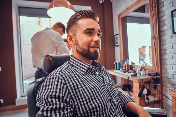 Attraente uomo curato è seduto in attesa di un barbiere presso il barbiere occupato — Foto Stock