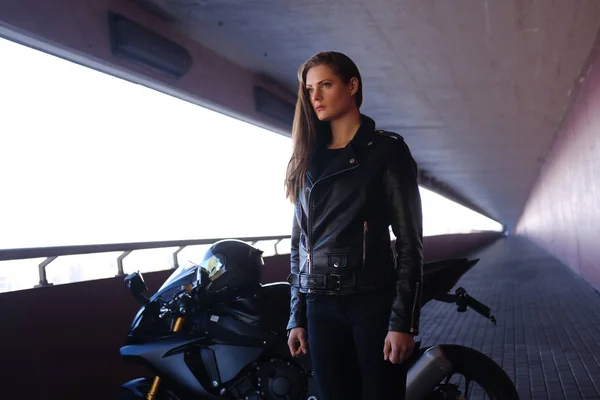 Bella donna pensierosa è in piedi in galleria con la sua moto e casco — Foto Stock