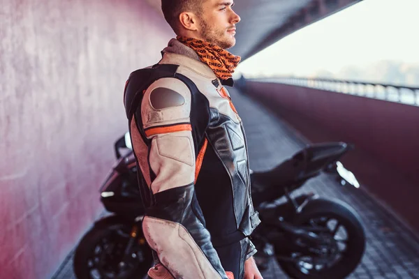 Young pensive biker is standing near his motobike in quiet tunnel — Stock Photo, Image