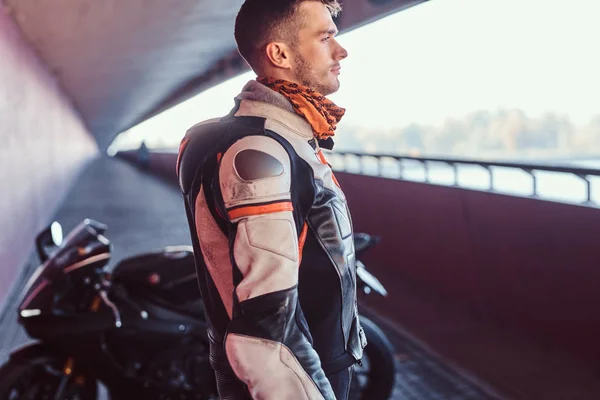 Jovem motociclista pensativo está de pé perto de sua moto em túnel silencioso — Fotografia de Stock