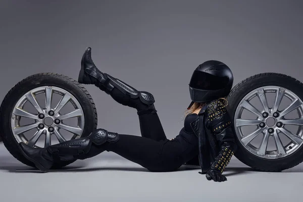 Moda, sport, ekstremalne. Rowerzysta dziewczyna ubrana w sprzęt motocyklowy, leżąc na podłodze z kołami samochodu w studio. — Zdjęcie stockowe
