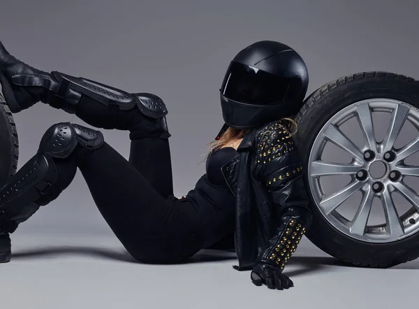 Moda, desporto, extremo. Menina motociclista vestindo equipamento de motocicleta deitado em um chão com rodas de carro em um estúdio . — Fotografia de Stock