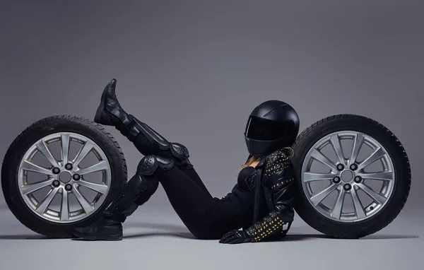 时尚, 运动, 极端。骑自行车的女孩穿着摩托车装备躺在地板上与汽车轮子在演播室. — 图库照片