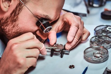 Expirienced clockmaster is fixing old watch for a customer at his repairing workshop clipart