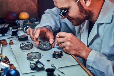 Expirienced clockmaster is fixing old watch for a customer at his repairing workshop clipart