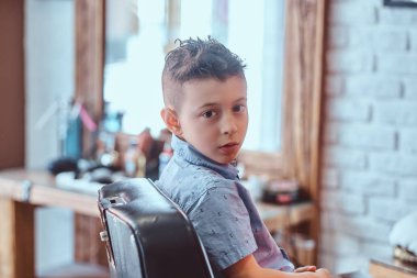 Güzel çocuk berber dükkanında otururken onun yeni saç modeli gösteriyor.