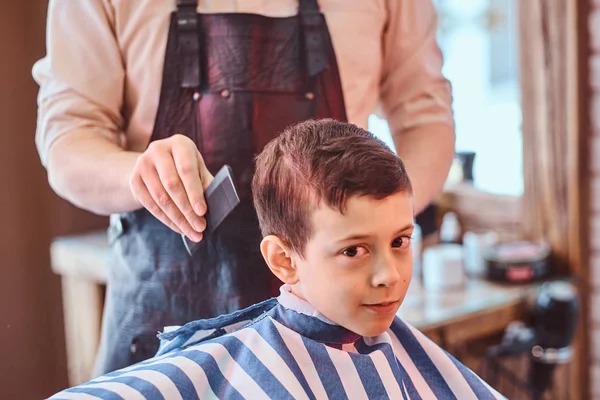 Pretty school boy had his first trendy haircut at modern barbershop.