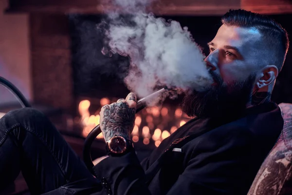 Porträt eines tätowierten bärtigen Mannes, der Wasserpfeife raucht und schönen Dampf macht — Stockfoto