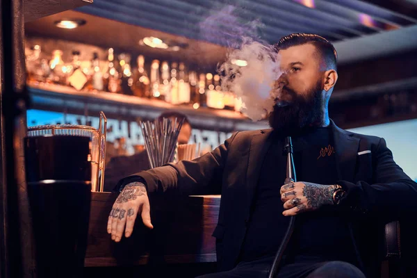 Portret van getatoeëerde bebaarde man die rook waterpijp, het maken van mooie damp — Stockfoto