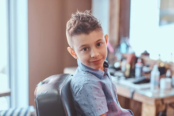 Mooie jongen toont zijn nieuwe kapsel terwijl zittend in Barbershop. — Stockfoto