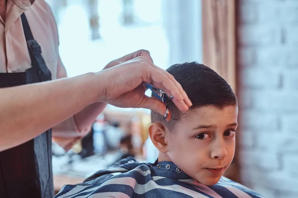 Engraçado menino está ficando moderno corte de cabelo de barbeiro expirienced na moda salão de cabeleireiro no firs tempo . — Fotografia de Stock