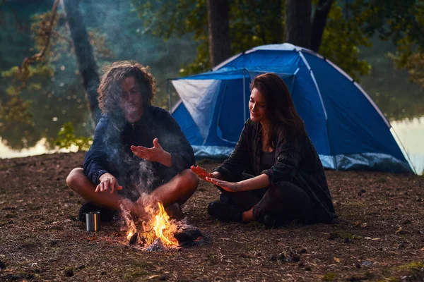 Attractive romantic couple is warming up near bonfire in the evening forest