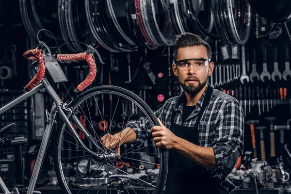 Atractivo hombre pensativo en gafas protectoras está reparando la bicicleta en su propio taller — Foto de Stock