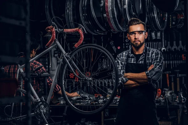 Gözlüklü yakışıklı adam kendi atölyesinde sabit bisiklet yanında duruyor. — Stok fotoğraf
