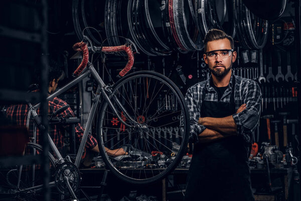 Handsome man in glasses is standing near fixed bicycle at his own workshop.