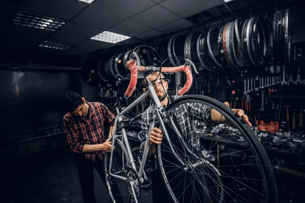 Два привлекательных человека работают над починкой велосипедов в занятой мастерской — стоковое фото