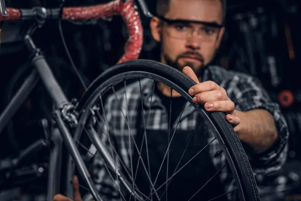 Guapo hombre serio en gafas protectoras es la fijación de la bicicleta en su propia tienda — Foto de Stock