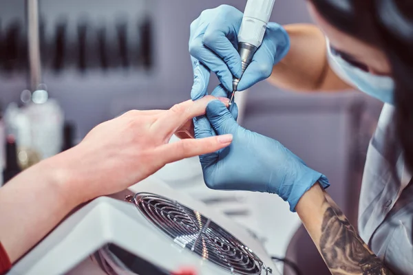 Mestre esteticista em luvas aplicando broca de unhas para aparar e remover cutículas. Manicura de hardware em um salão de beleza — Fotografia de Stock