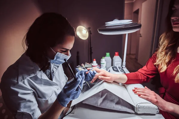 Esteticista haciendo largas uñas artificiales transparentes a una clienta femenina. Procedimiento de manicura en un salón de belleza —  Fotos de Stock