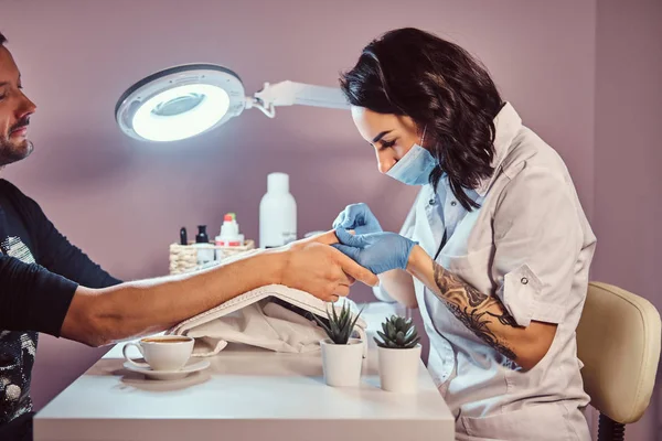 Un homme avec un tatouage sur la main recevant une manucure par un esthéticien dans le salon de beauté. Gros plan mains — Photo